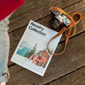 Person wearing a red coat and light blue jeans standing next to a magazine titled 'Revelry Collection' on a wooden surface.